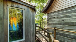 Una cabaña de madera con una ventana que refleja árboles, una terraza de madera y una estructura tipo cabaña de troncos.