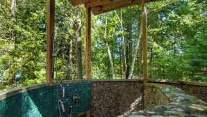 Una estructura de madera con un muro de piedra y un grifo de metal, rodeada de un bosque.