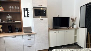 A modern hotel room with a kitchenette, a flat-screen TV, a bed with a leaf-patterned duvet, and a wooden floor. - Cocooning in Cognac (Cognac)