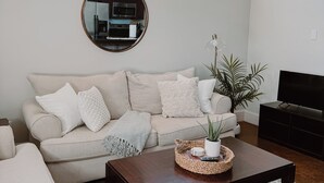 Un salon avec un canapé, une table basse et un téléviseur. Il y a des fenêtres et un miroir sur le mur.
