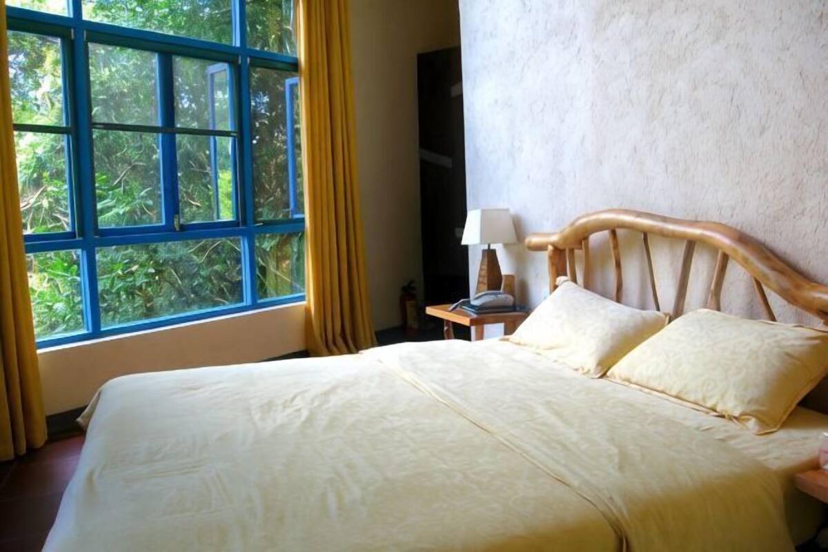 Una cama con cabecera de madera, una mesita de noche con lámpara y una ventana con cortinas.