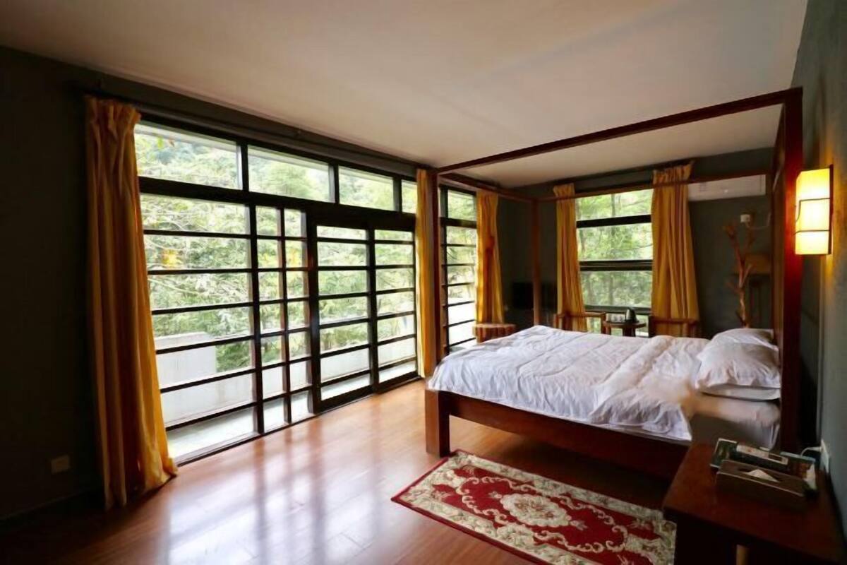 Un dormitorio con un ventanal grande, una cama, una mesita de noche y una alfombra roja con diseño.