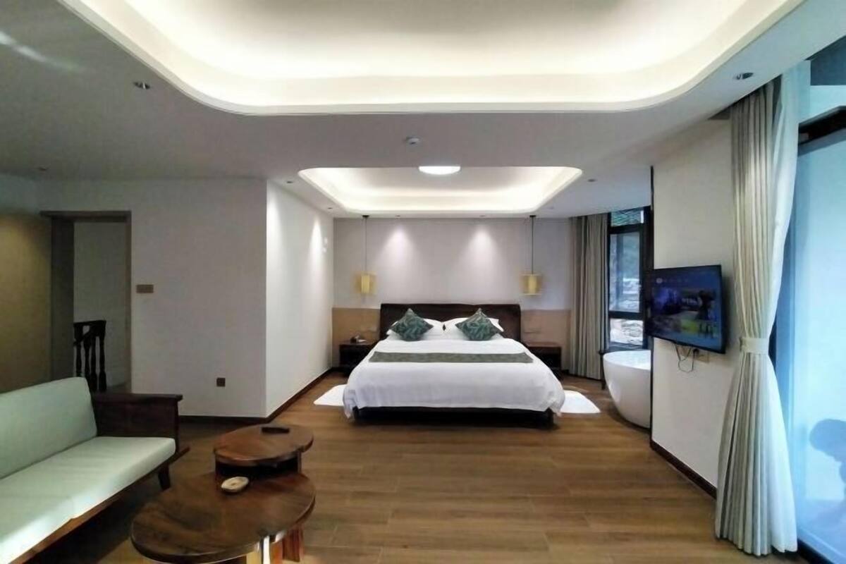 Una habitación de hotel moderna con una cama grande, un sofá, una mesita y un televisor en la pared.