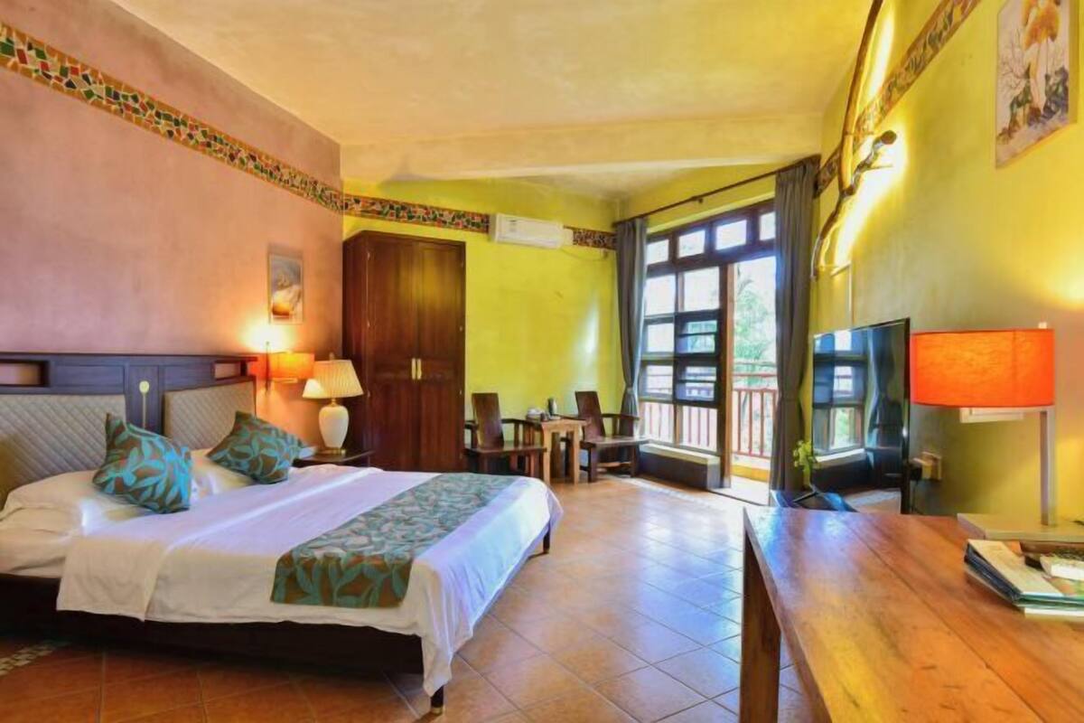 Habitación de hotel con cama, mesita de noche, lámpara, televisión y vistas al exterior.
