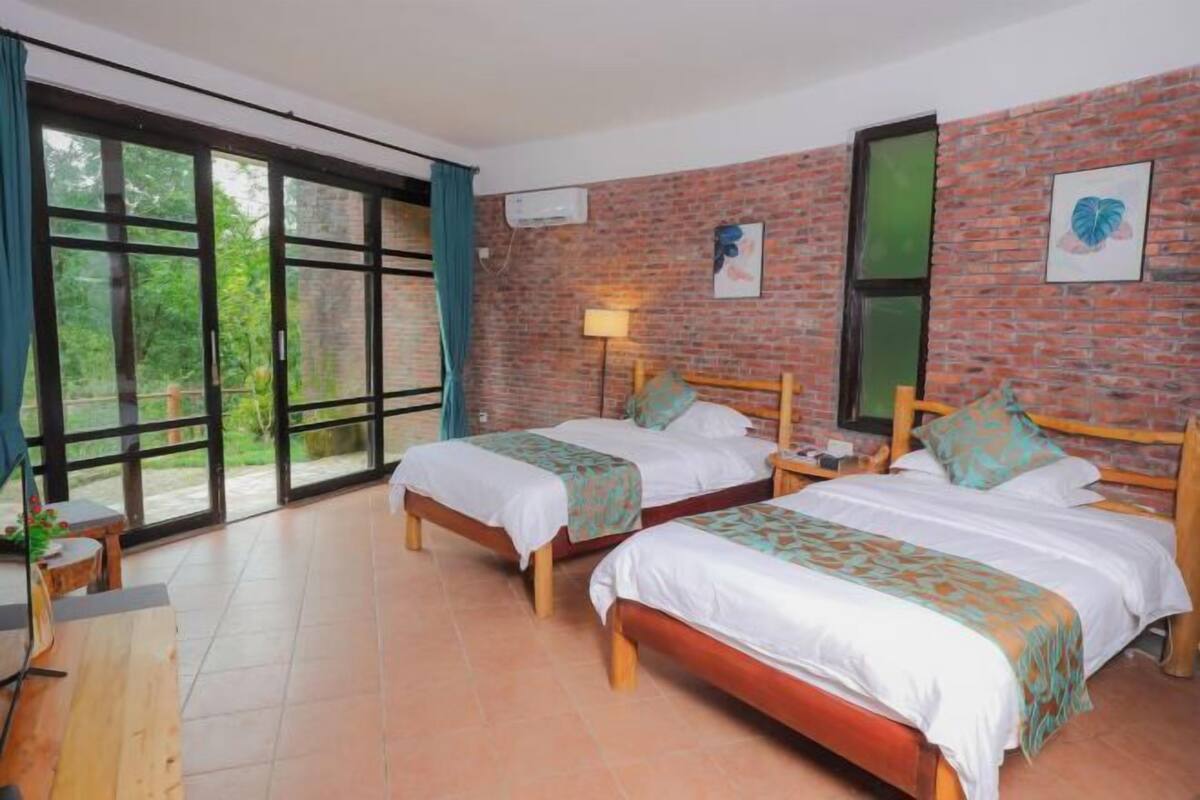 Una habitación con dos camas de madera, una pared de ladrillo y un amplio ventanal con cortinas.