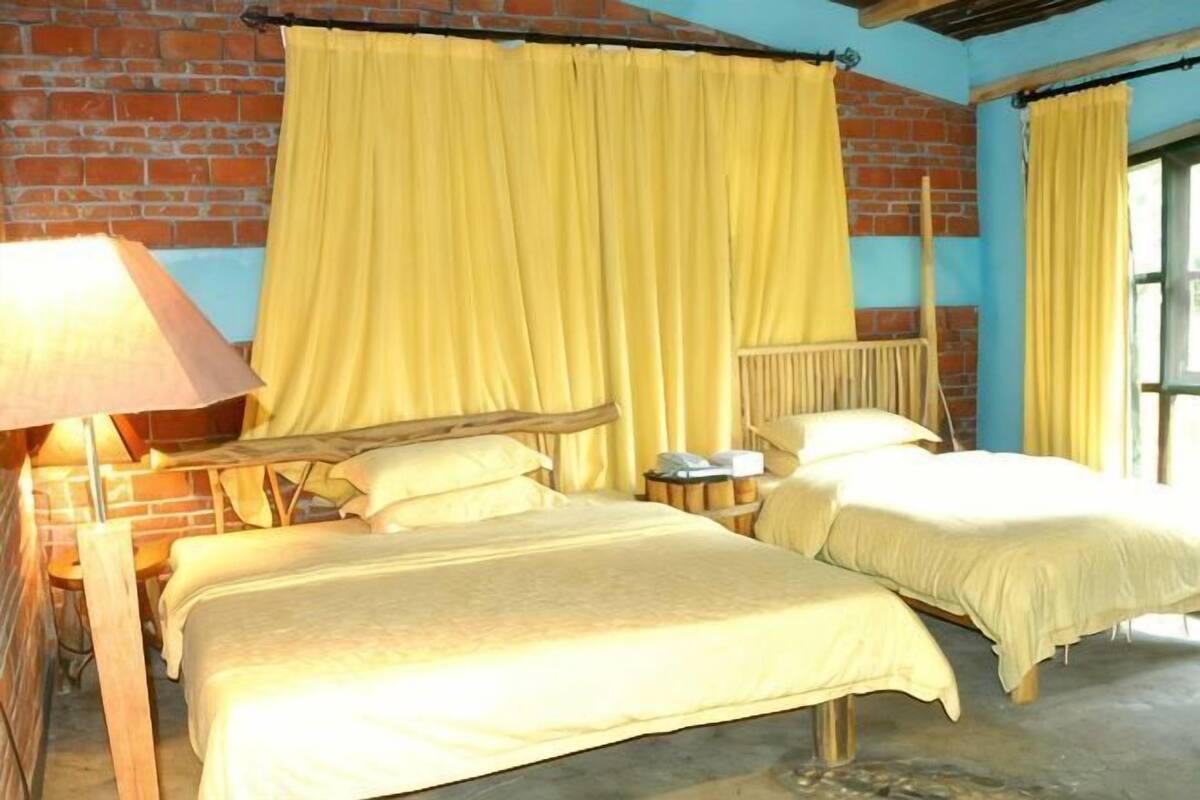 Una habitación con dos camas, una pared de ladrillo y cortinas amarillas.