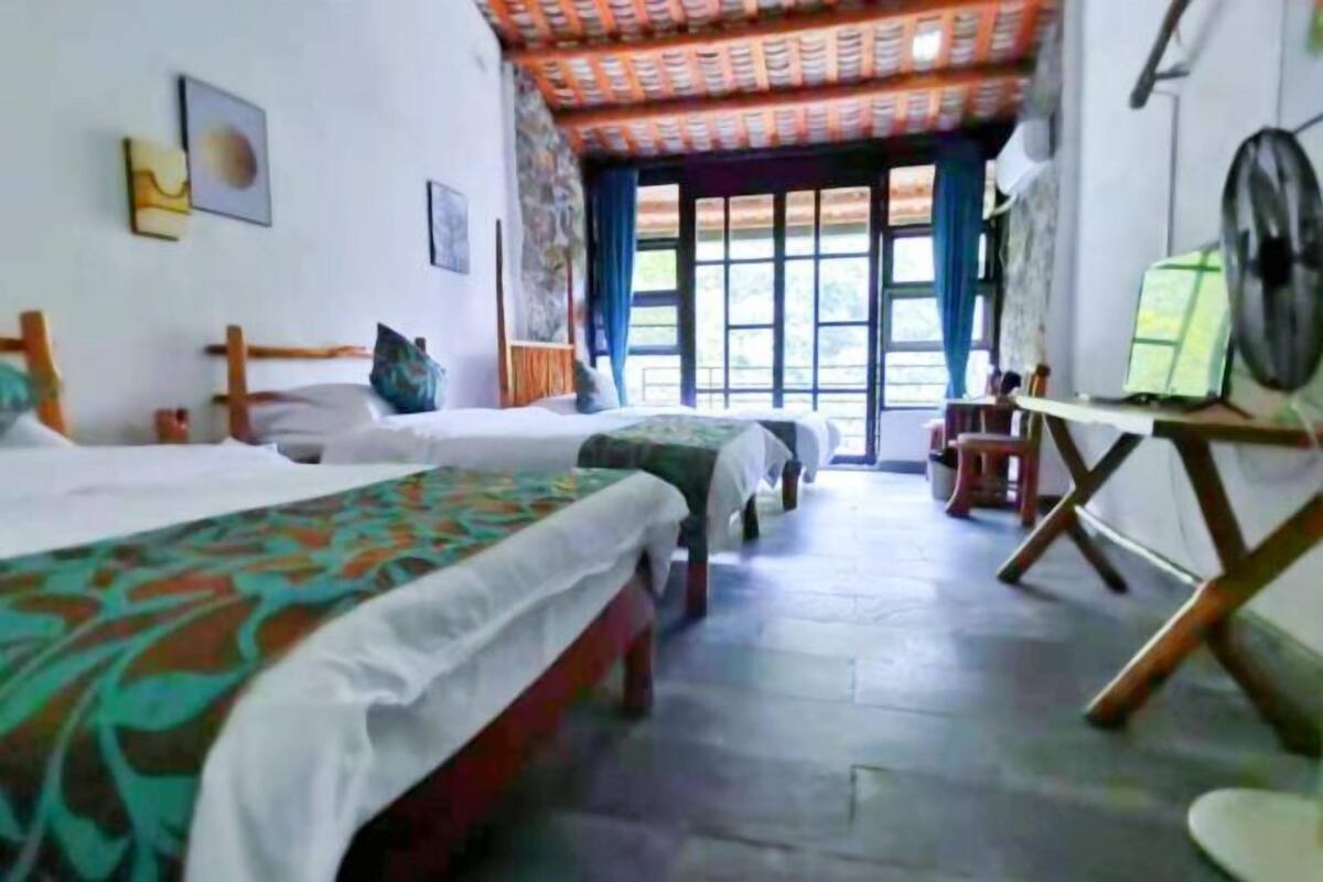 Una habitación con dos camas, una mesita pequeña y un ventilador.