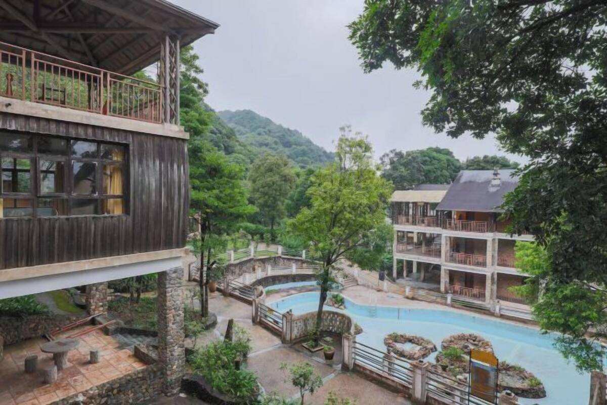Un hotel de varios pisos con área de piscina, senderos de piedra y abundante vegetación.