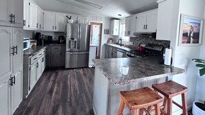 Una cocina moderna con armarios blancos, electrodomésticos de acero inoxidable, encimera de granito y taburetes de madera.