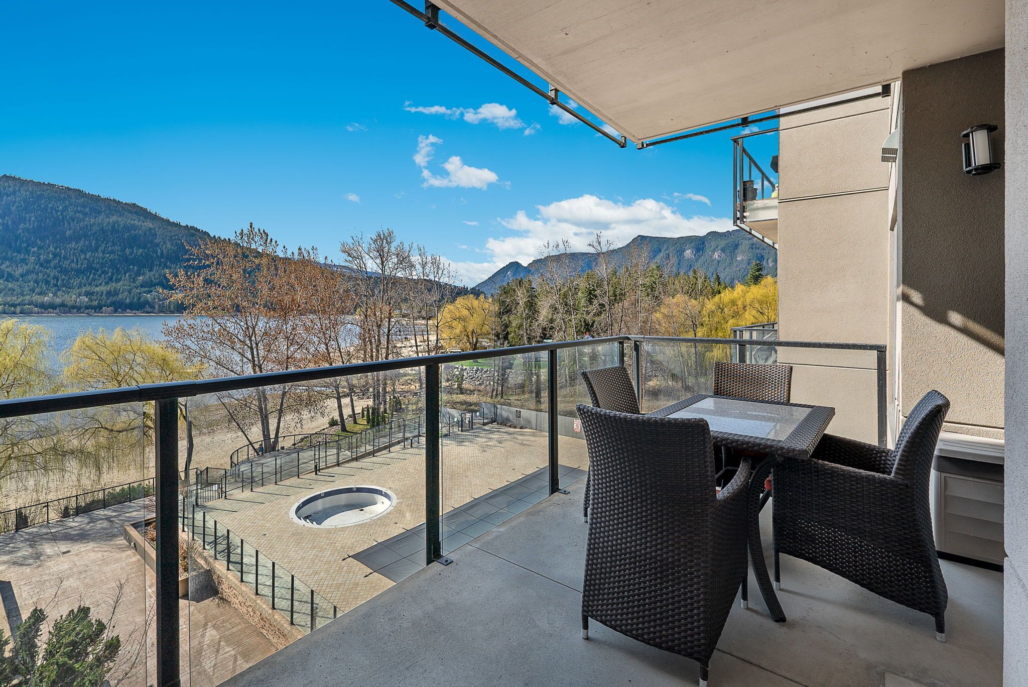 A balcony with wicker furniture overlooking a lake and mountains.
