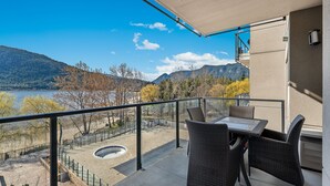 Un balcon meublé avec des meubles en osier, donnant sur un lac et des montagnes.
