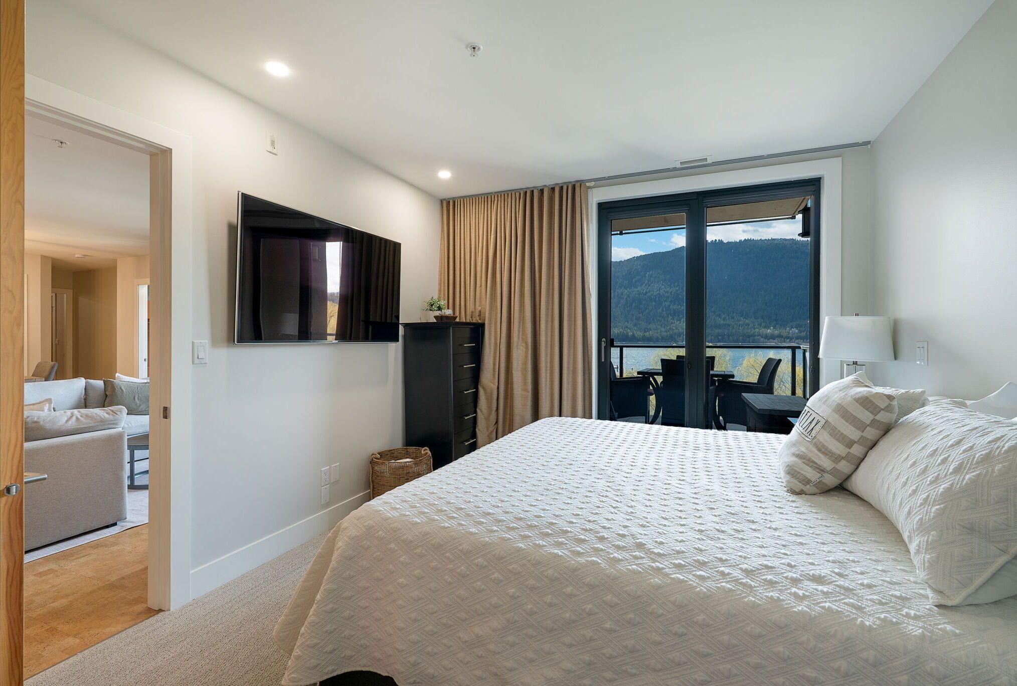 Une chambre avec un grand lit, un téléviseur fixé au mur, une fenêtre avec des rideaux et une vue sur l’extérieur.
