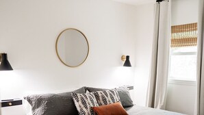 Ein Schlafzimmer mit einem Bett, einem Deckenventilator, einem runden Spiegel und einem Fenster mit Vorhängen.