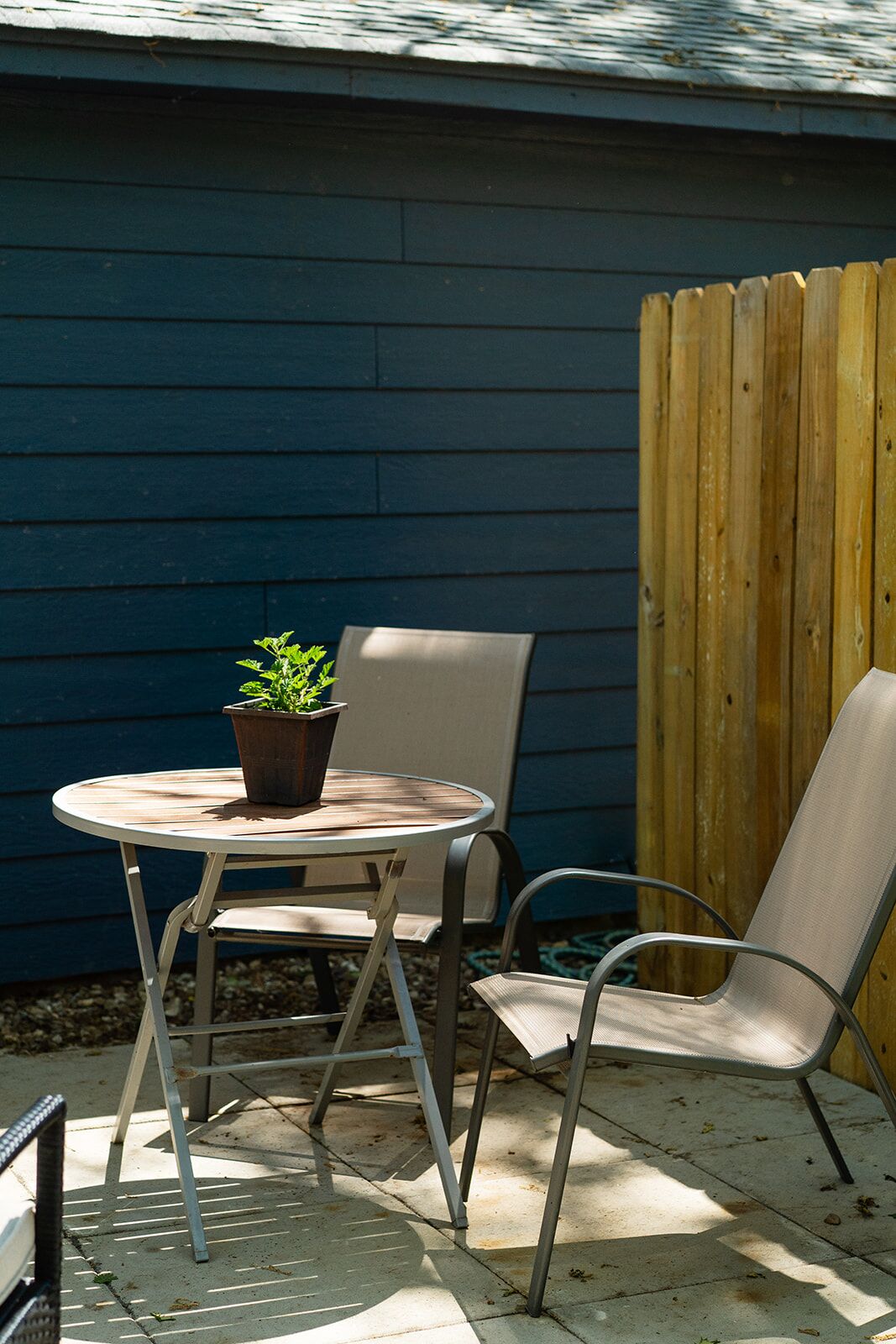 Une terrasse avec une table ronde et deux chaises, un pot de fleurs et une clôture en bois.