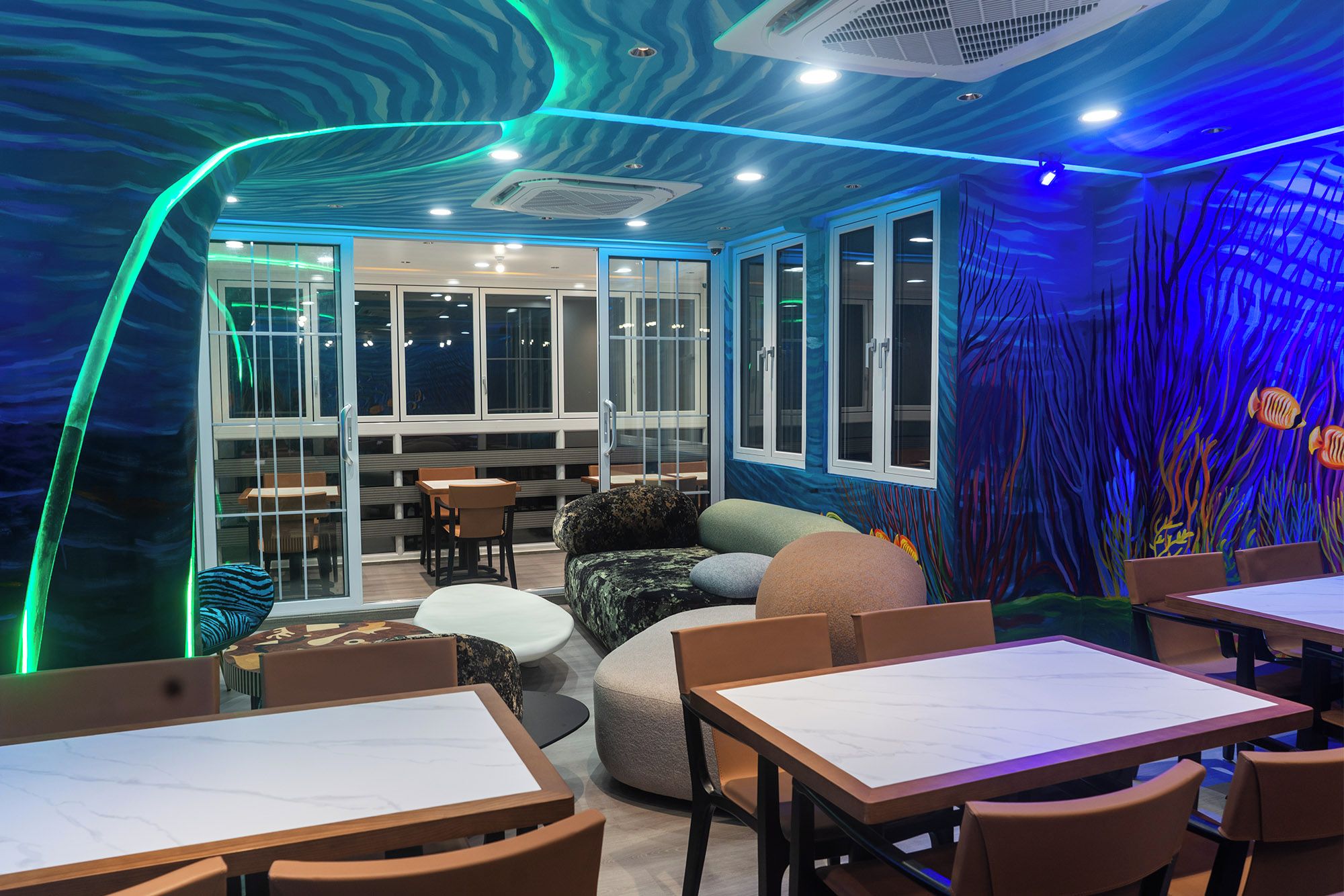 A restaurant interior with a modern design, featuring a seating area with tables and chairs, a large window, and a wall with an underwater mural.