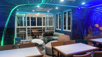 A restaurant interior with a modern design, featuring a seating area with tables and chairs, a large window, and a wall with an underwater mural.