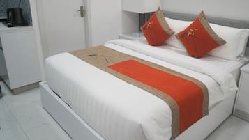 Una cama bien hecha con ropa blanca y dos almohadas rojas, una manta roja y una mesita de noche con una lámpara.