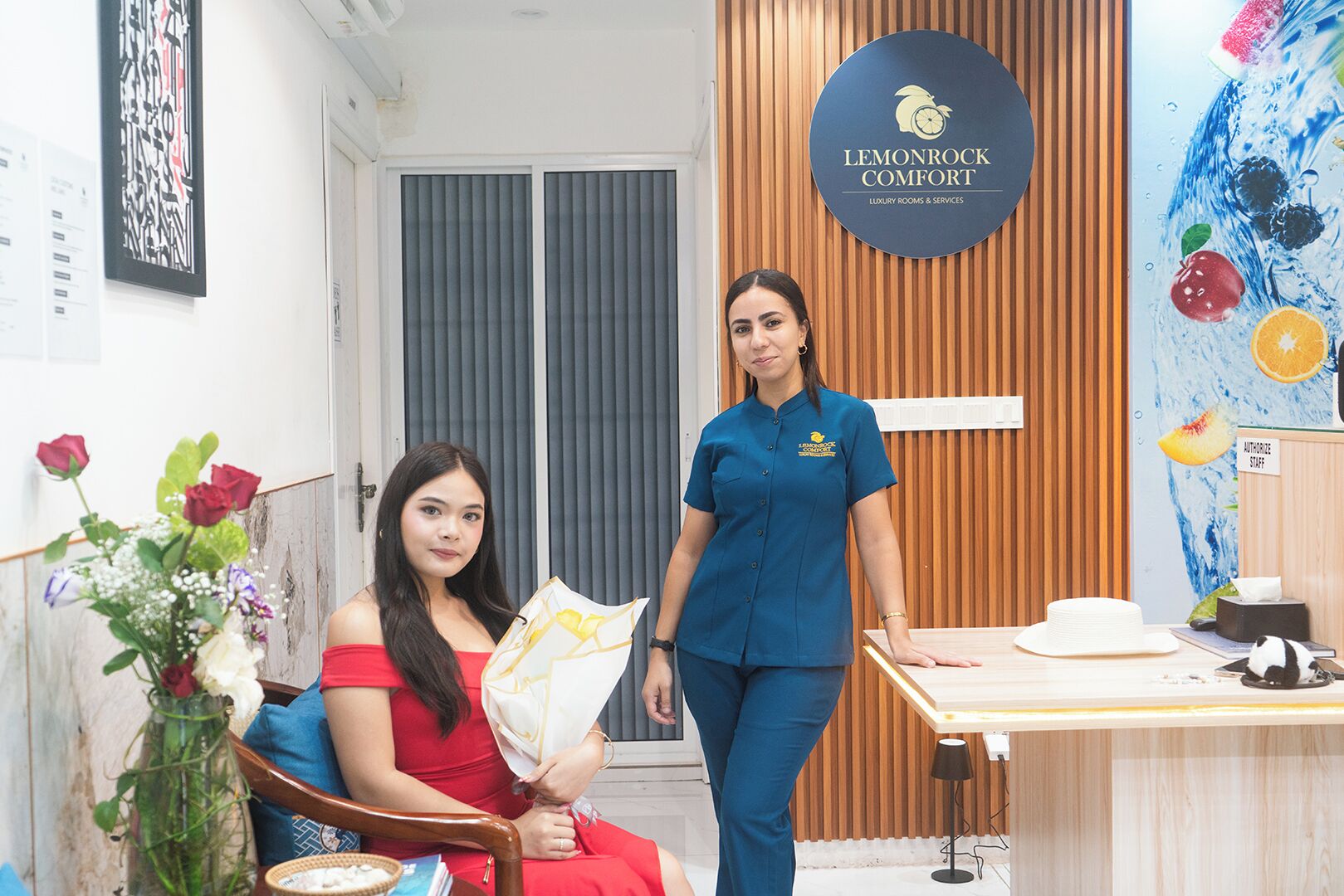 A reception area with a wooden desk, a chair, and a wall-mounted sign reading "LEMONROCK COMFORT LUXURY ROOMS & SERVICES".