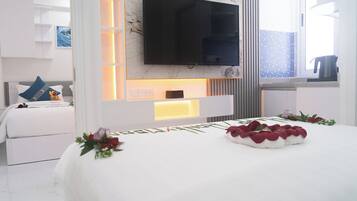 A modern hotel room with a large bed, a flat-screen TV mounted on the wall, and a bedside table with a lamp.