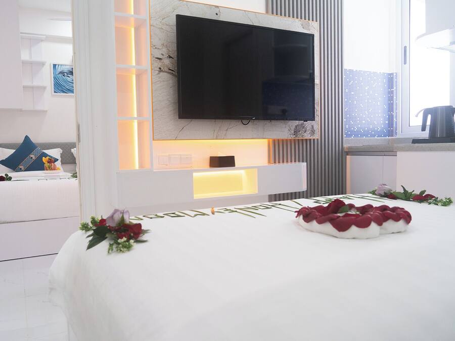 A modern hotel room with a large bed, a flat-screen TV mounted on the wall, and a bedside table with a lamp.