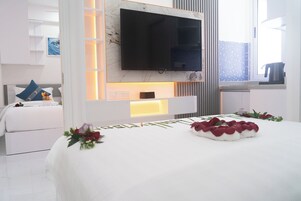 Una habitación de hotel moderna con una cama grande, un televisor de pantalla plana en la pared y una mesita de noche con lámpara.