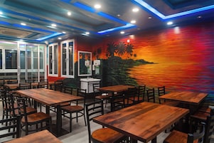 A restaurant interior with wooden tables and chairs, a mural of a sunset, and a view of the sea.