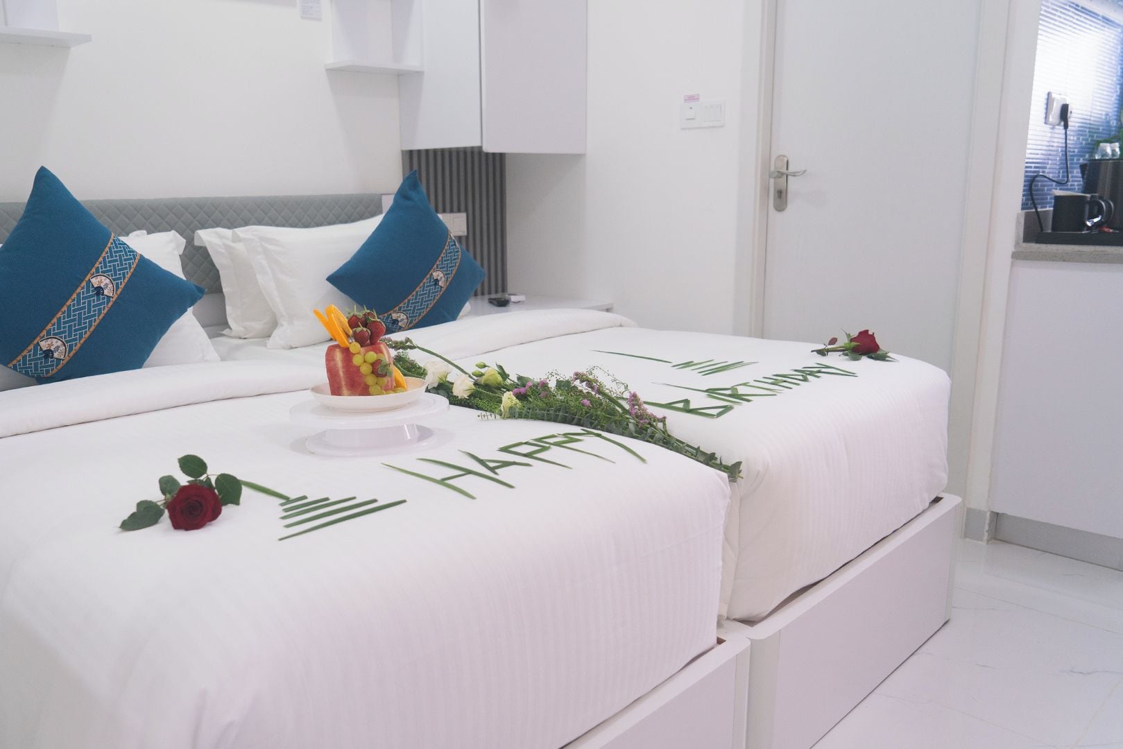 A neatly made bed with a birthday greeting and a fruit arrangement.