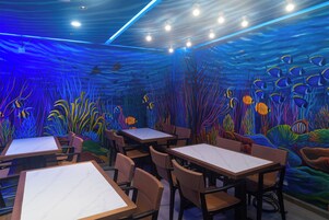 Un comedor interior con mesas y sillas, decorado con un mural submarino.