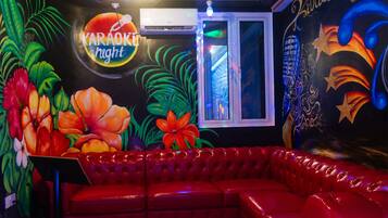 A room with a red leather couch, a karaoke sign, and tropical wall art.