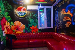 A room with a red leather couch, a karaoke sign, and tropical wall art.