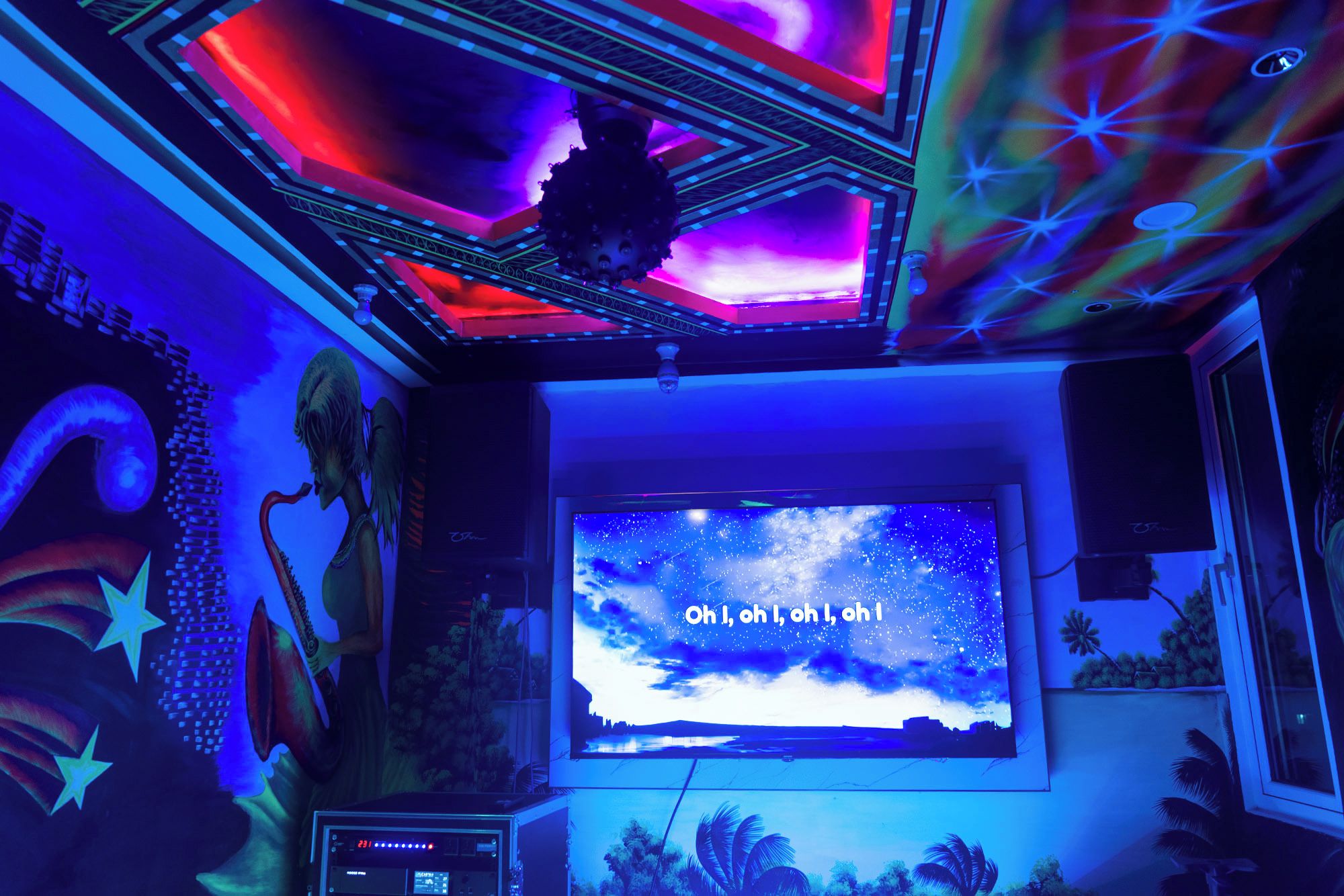 Ein Zimmer mit einem großen Bildschirm, der einen Sternenhimmel zeigt, einer Musikanlage und einer Decke mit geometrischem Muster.