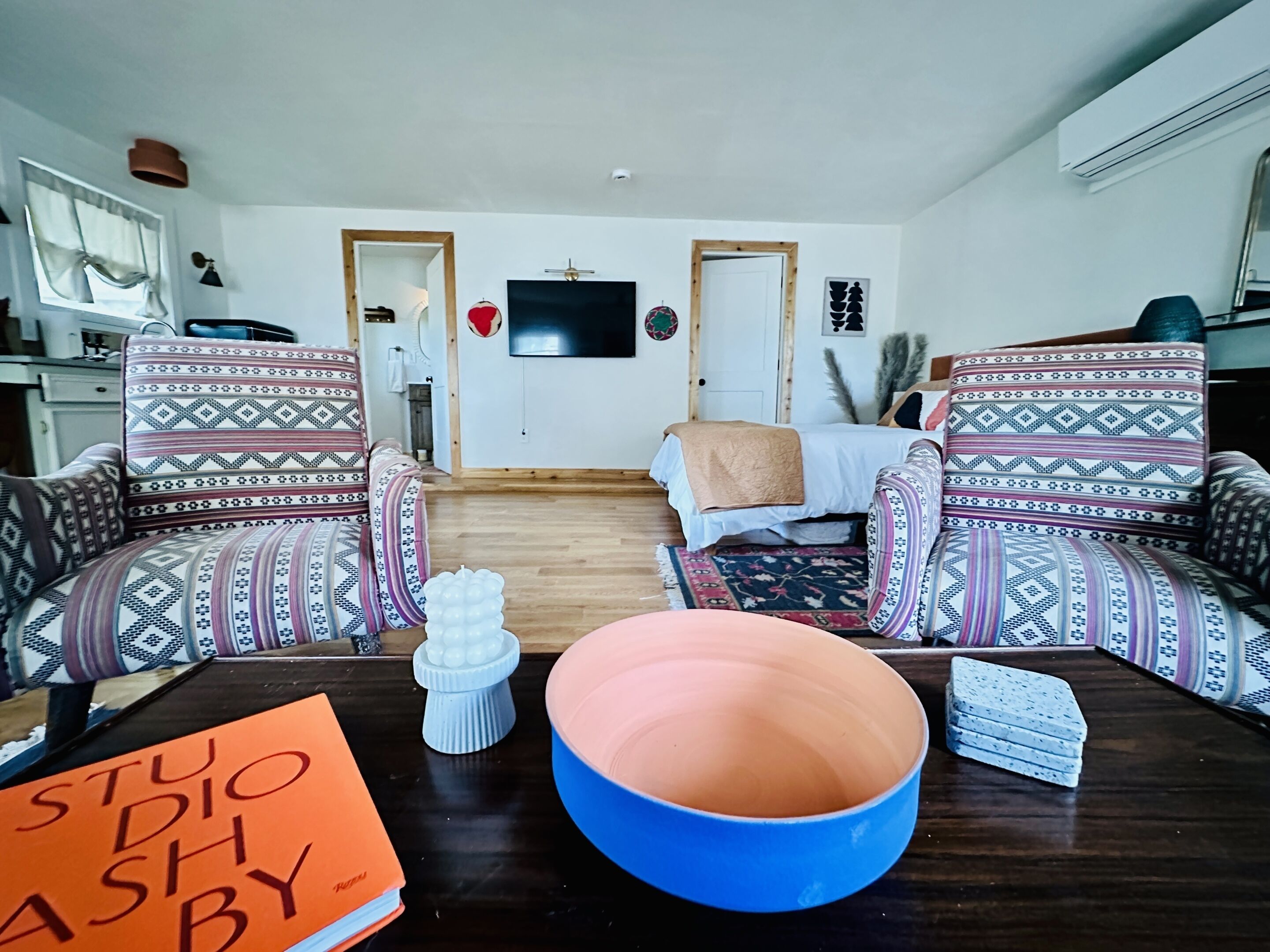 A living room with patterned armchairs, a coffee table with a bowl, and a bed with a blanket.