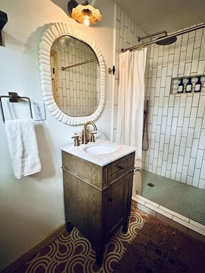 Un baño con un espejo redondo, un lavamanos y una ducha.