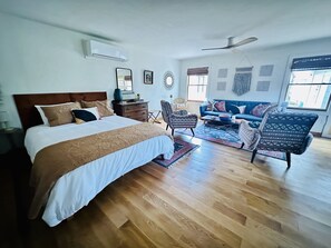 Un dormitorio con una cama grande, un sofá, dos sillones estampados, una mesa de centro y un ventilador de techo.