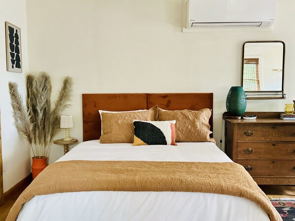 Una cama bien hecha con cabecera marrón, una lámpara de noche y almohadones decorativos.