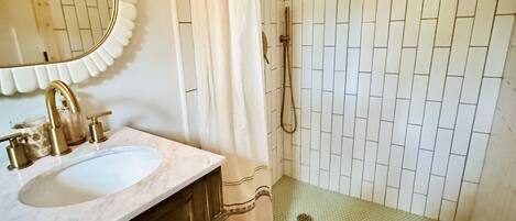 A bathroom with a white tiled shower, a sink with a marble countertop, and a mirror with a scalloped edge.