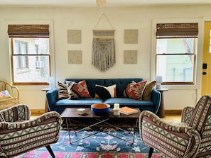 A cozy living room with a blue sofa, patterned armchairs, a coffee table, and a colorful rug.