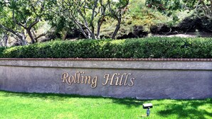 Letrero que dice 'Rolling Hills' sobre una pared de concreto con un área verde al frente.