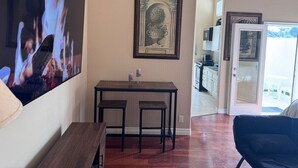 Un comedor con una mesa de madera y dos sillas, una obra de arte enmarcada sobre la mesa, y un televisor mostrando una escena de fuego.
