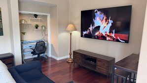 Una sala de estar con una televisión de pantalla plana, un sofá, una mesa de centro, una lámpara y un mueble para televisión.