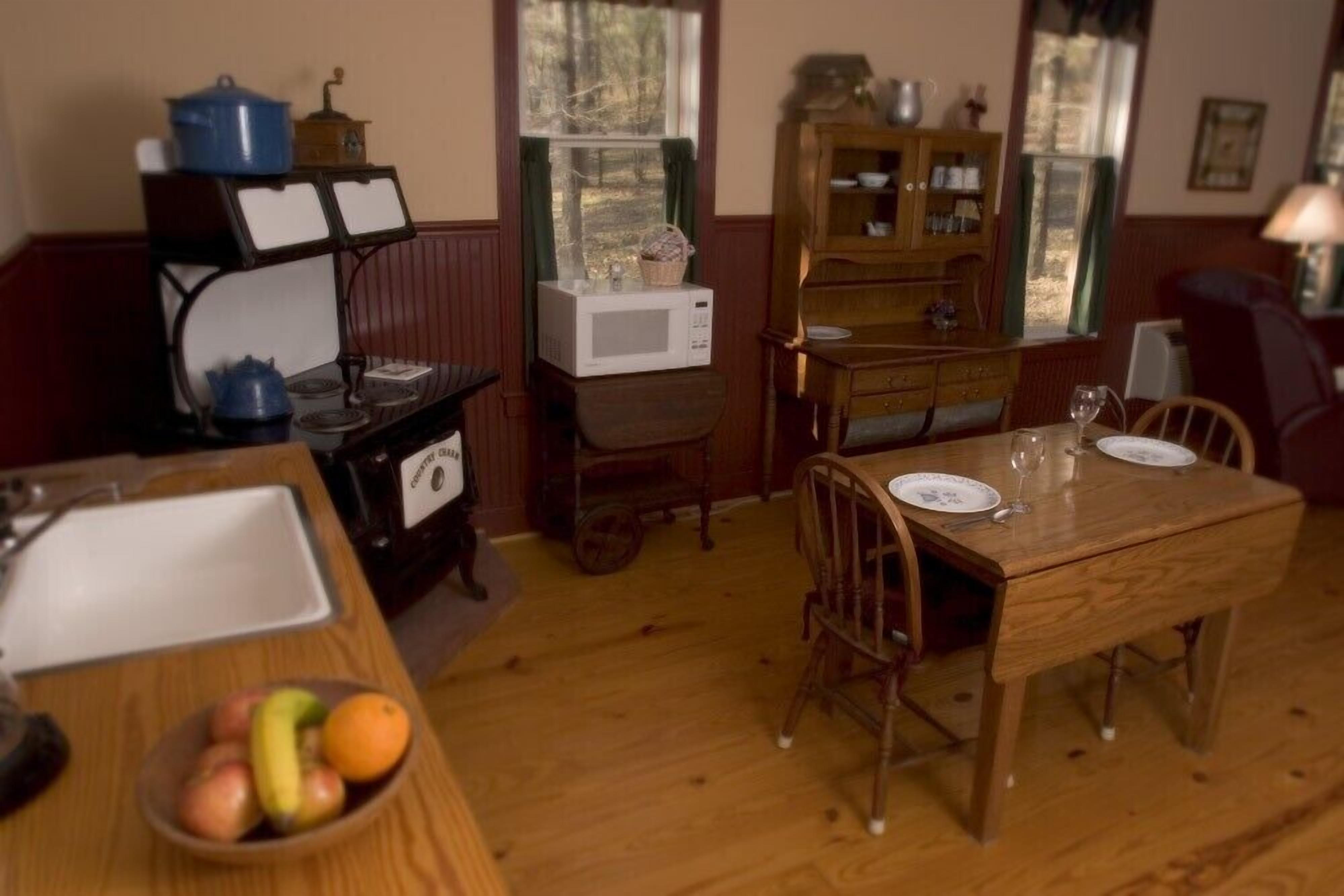 A dining area with a wooden table set for two, a kitchen area with a microwave and a stove, and a cabinet with dishes.