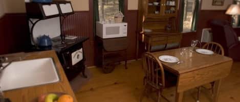 A dining area with a wooden table set for two, a kitchen area with a microwave and a stove, and a cabinet with dishes.