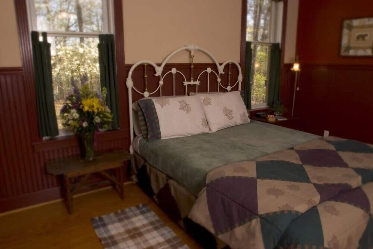 A bedroom with a bed, a bench, a window with curtains, and a bedside table.