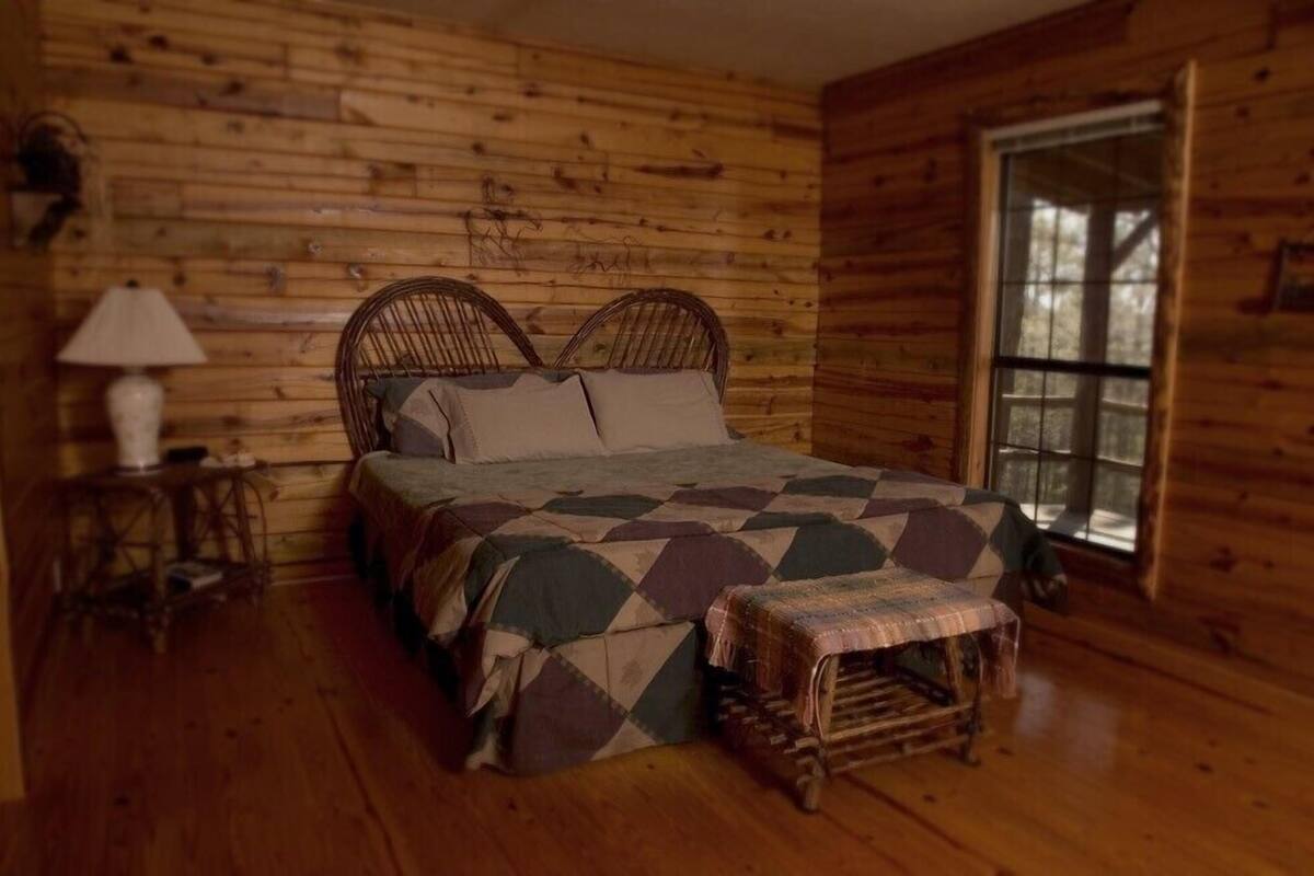 A wooden cabin room with a bed, a lamp, and a window.