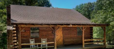 A rustic log cabin with a porch, a wooden bench, and a table.
