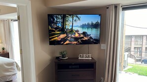 Una sala de estar moderna con un televisor de pantalla plana montado en la pared, una mesa de centro de madera con un juego, y vista a un lago a través de un ventanal grande.