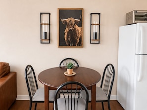 A dining area with a round table, four chairs, a potted plant, and a framed animal picture.