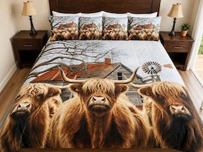 A bed with a large, detailed print of highland cattle and a windmill, flanked by matching pillows and a matching duvet cover.