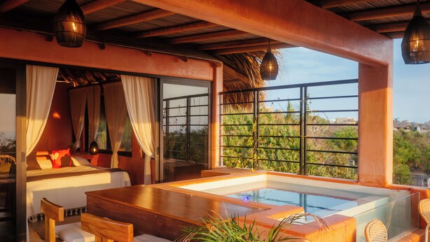 A modern room with a large window, a wooden table, and a hot tub. - Penthouse with pool & ocean view (Puerto Escondido)