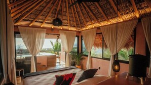 A bedroom with a large bed, a view of the ocean, a thatched roof, and a balcony with a table and chairs. - Penthouse with pool & ocean view (Puerto Escondido)